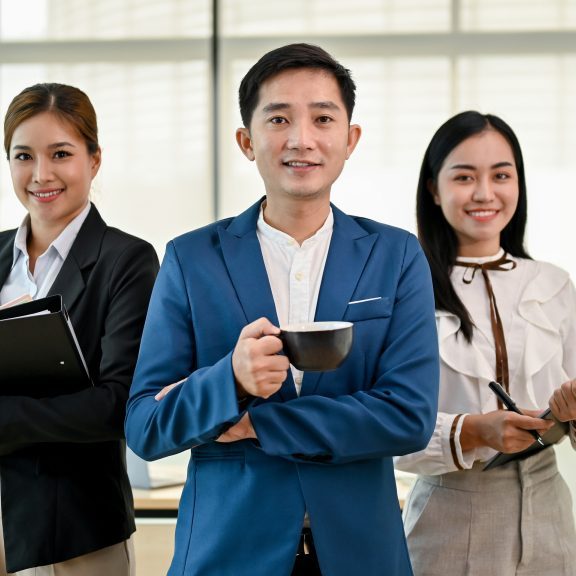 A portrait of professional and confident millennial Asian businesspeople is standing in the office, smiling and looking at the camera.